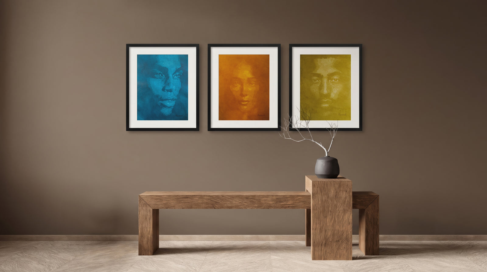 Three framed Khabraal portrait paintings in blue, orange, and olive tones grouped on a brown wall above a wooden bench — trade program installation example